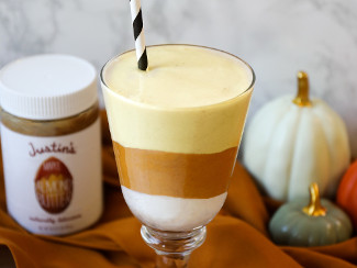 A parfait glass containing the Candy Corn Smoothie, flanked by pumpkins and a jar of Justin's Maple Almond Butter.