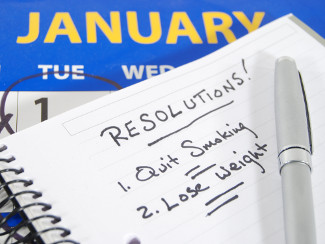 List of New Year's resolutions on a notepad in front of a calendar.